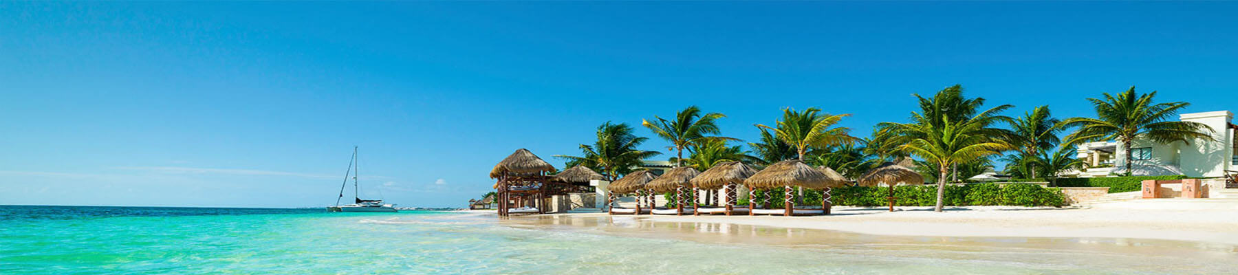 Picture of a beautiful beach in Cancun, Mexico.  The picture shows tall palm trees, a sandy beach, blue water and a blue sky.