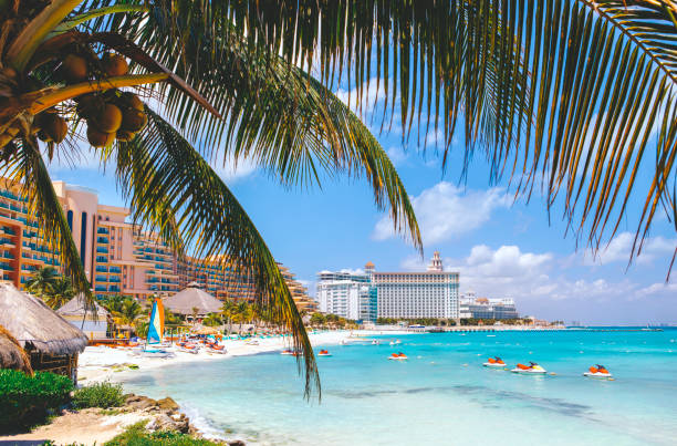 Picture of a beautiful sandy beach in Cancun, Mexico.  The picture shows white sand, blue water, nice resorts and jet skies in the ocean.