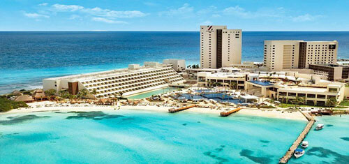 Picture of a beautiful sandy beach in Cancun, Mexico. The picture shows small boats near the shore line and grass huts on the beach.