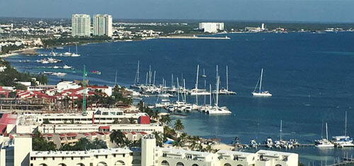 Picture of a beautiful harbor and beach line in Cancun, Mexico.  The picture shows, boats in the harbor, blue skies and blue water.