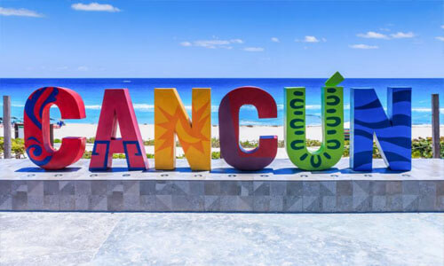 Picture of a street sign with the words “Cancun” in beautiful Cancun, Mexico.  The sign is very colorful with various shades of color hand-painted on the letters.