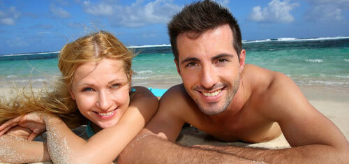 Picture of a smiling couple showing their happiness with their visit to Cancun for plastic surgery.  The woman is resting her head on her arm and both are facing the camera with a big smile.