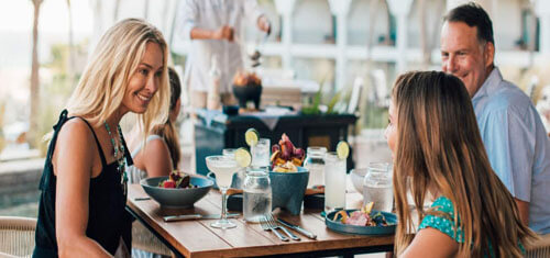 Picture of a happy guest dining in Cancun, Mexico.  The picture is of an attractive woman with long sandy blonde hair, wearing a black blouse, and sitting at a table with companions.