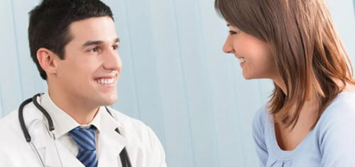 Picture of a smiling patient consulting with a smiling plastic surgeon in Cancun, Mexico.  The patient is wearing a light blue shirt and the doctor is wearing a white smock