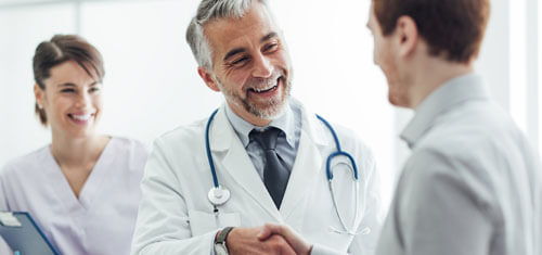 Picture of a happy patient shaking hands with a Cancun plastic surgeon.  The picture also shows an assistant looking on.