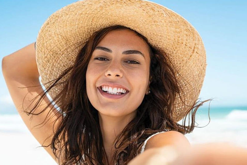Picture of a on the beach, happy with her plastic surgery at Costa Rica MedVentures.  The woman is wearing tan sun hat and sitting on a Costa Rica beach.