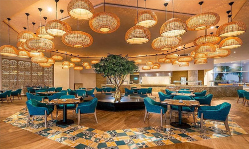 Picture of an elegant hotel lobby in Cancun, Mexico.  The picture shows an ornate ceiling with golden lighting and blue tables and chairs.