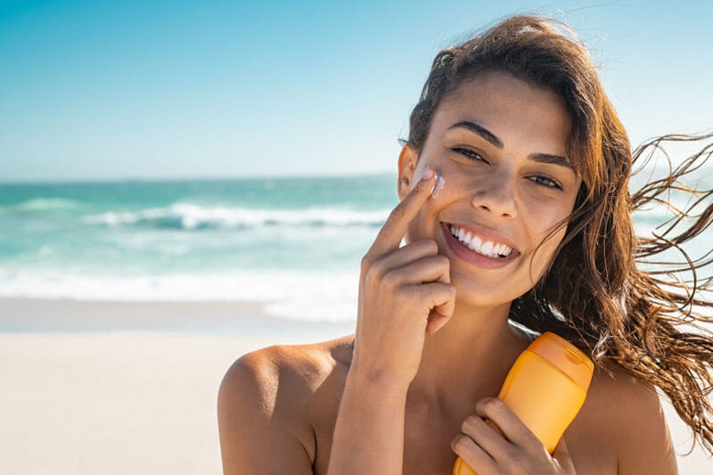 Picture of a smiling woman, happy with her nose surgery she had at Costa Rica MedVentures.  The woman has long brown hair and is standing on a sandy Costa Rica beach with the ocean in the background.