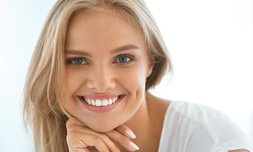 Picture of a beautiful woman, happy with her face lift procedure in Cancun, Mexico.  The woman has long blonde hair, is looking directly into the camera and is holding her right hand to her chin highlighting her face lift.