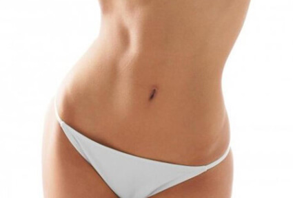 Picture of a woman facing the camera and happy with the perfect abdomen liposuction procedure she had with top plastic surgeons in beautiful Cancun, Mexico.  She is wearing a two-piece bikini and showing a flat abdomen to the camera.