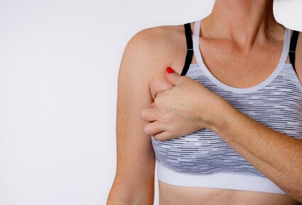 Picture of a woman facing the camera and happy with the perfect bra line liposuction procedure she had with top plastic surgeons in beautiful Cancun, Mexico.  The woman is wearing a soft light purple pastel top and holding one hand to the area of her bra line liposuction.