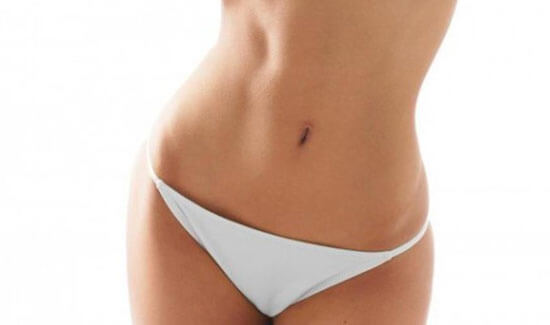 Picture of a woman facing the camera and happy with the perfect abdomen and waist liposuction procedure she had with Cancun MedVentures in beautiful Cancun, Mexico.  She is wearing a two piece bikini and showing a flat abdomen to the camera.