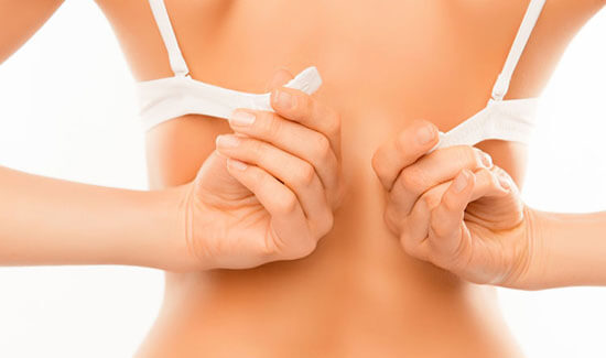 Picture of a woman with her back to the camera and happy with her perfect bra line liposuction procedure she had with Cancun MedVentures in beautiful Cancun, Mexico.  The woman attaching the ends of a bra strap showing the results of her bra line liposuction.