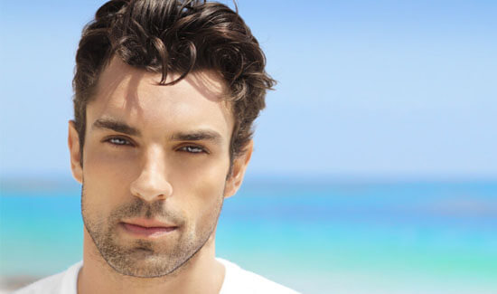 Picture of a man, facing the camera and happy with his perfect hair transplant procedure he had with Cancun MedVentures in beautiful Cancun, Mexico.  The man has a white t-shirt on and has a blue ocean as a backdrop.