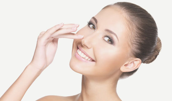 Picture of a woman, facing the camera and happy with her perfect nose surgery procedure she had with Cancun MedVentures in beautiful Cancun, Mexico.  The woman has her hand to the side of her nose and is pointing to where she had the surgery.