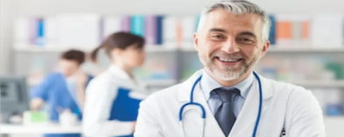 Picture of a plastic surgeon representing the doctors at Top Plastic Surgeons in Cancun, Mexico.  The picture shows a doctor in a white coat with a stethoscope around his neck and arms crossed, looking directly at the camera and smiling.