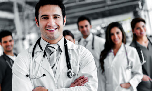 Picture of a group of doctors and assistants representing top plastic surgeons in Cancun, Mexico.  Five are standing in the back and one is standing in front of them with arms folded.